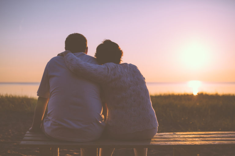Two people sitting together on a bench by the water